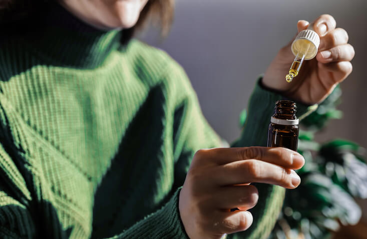 A woman holding a dropper of sublingual CBD cannabis hemp oil after completing her cannabis education