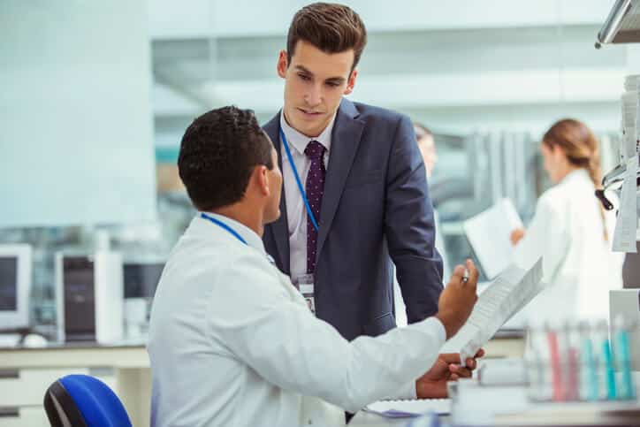 A male RA associate discussing procedures with a laboratory technician after completing his regulatory affairs training
