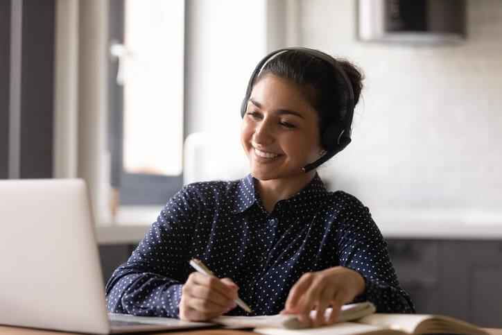A happy female pharmaceutical professional writing on a notepad while receiving online pharmaceutical training 
